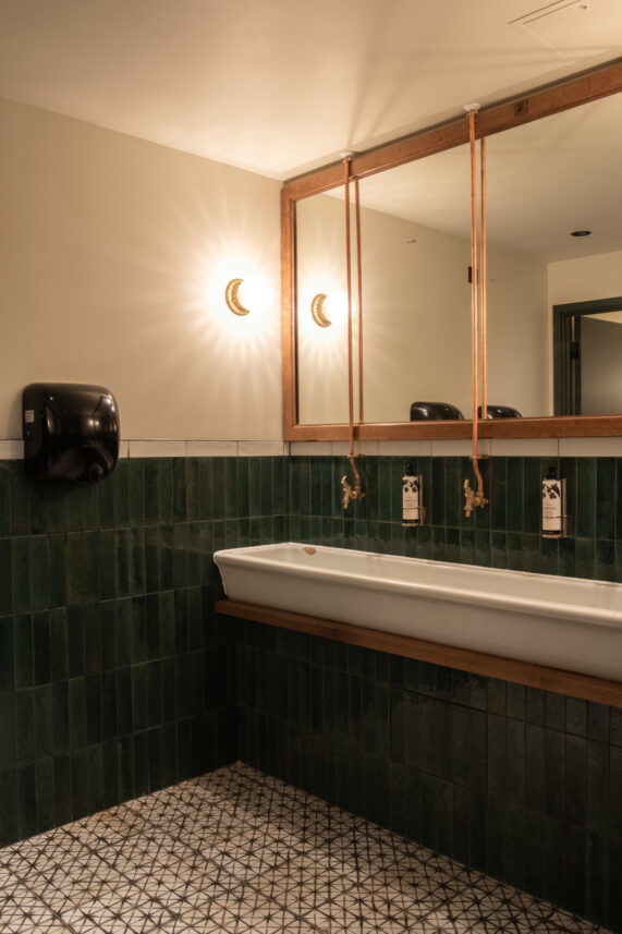 Bathroom sink with mirrors and stylish green tiles on the wall and patterned tiles on the floor