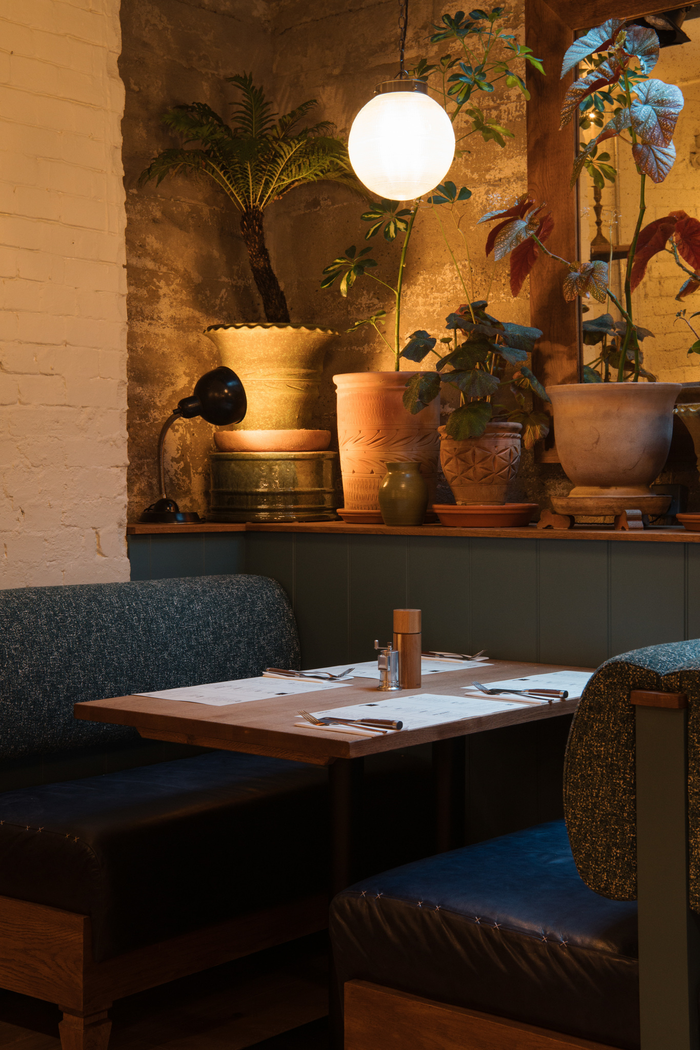 Banquette with leather upholstery with warm lighting, exposed bricks and lots of plants.