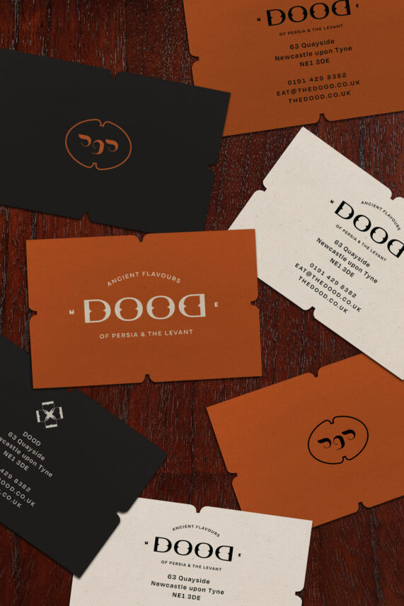 DOOD restaurant custom business cards design in orange, cream and black on a wooden surface